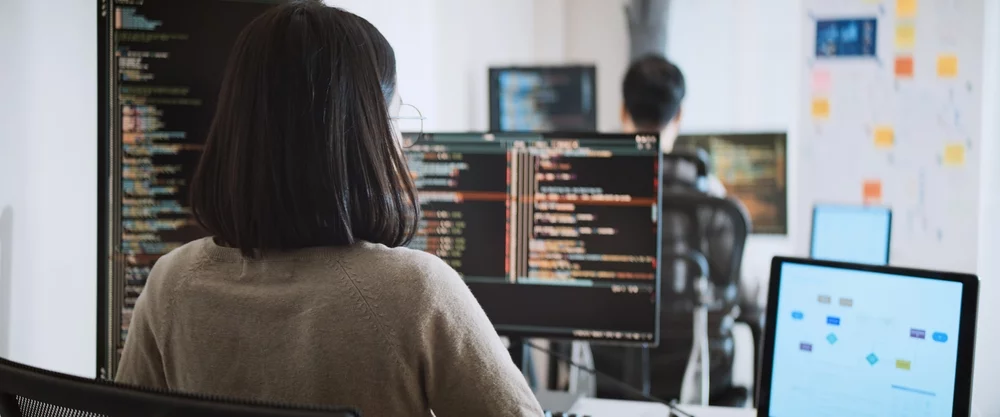 Two coders working on multiple computer screens.
