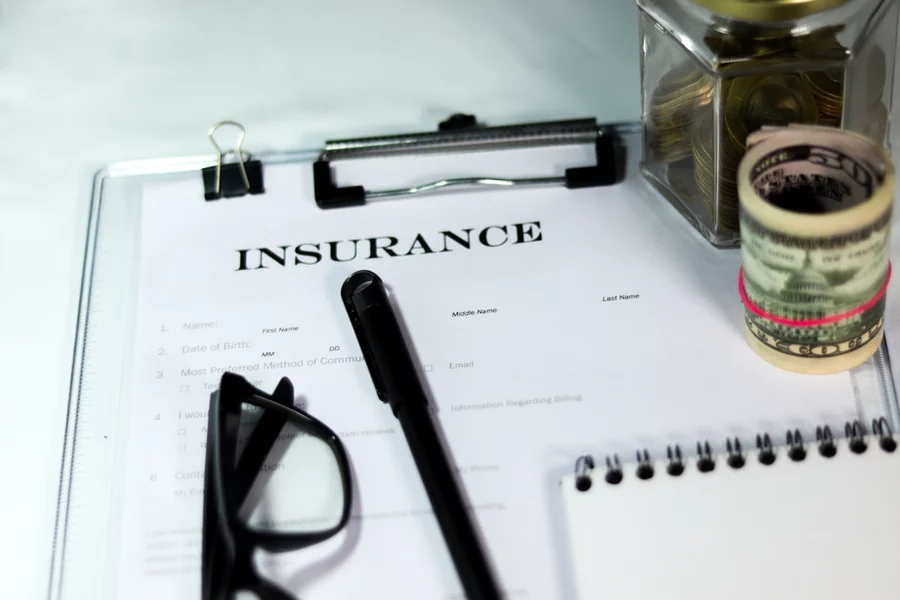 Insurance form with can of coins and dollar bundle with a pen and eyeglass